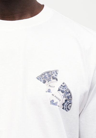 Γραφικό σχισμένης μπλε και λευκής πορσελάνης πιάτου με λουλουδένια σχέδια και μερικό κείμενο σε λευκό μπλουζάκι με στρογγυλή λαιμόκοψη.