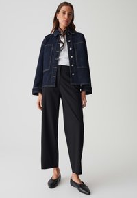 Veste en denim foncé avec de grandes poches, boutons argentés, associée à un pantalon noir et des ballerines noires. Présente un haut blanc et une écharpe à motifs.