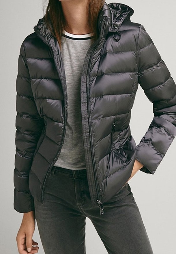 Giubbotto a vento nero con cappuccio, caratterizzato da una texture trapuntata, zip frontale e tasche laterali. Indossato sopra una T-shirt grigia.