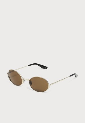 Lunettes de soleil de forme ovale avec fines montures en métal argenté et verres teintés marron, embouts en plastique noir sur les branches, présentées sur fond blanc.