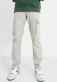 Lichtgrijze cargobroek met zijzakken, voorzien van een slim fit ontwerp, gestikte details en gecombineerd met groene en witte sneakers.
