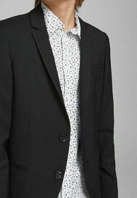 Černý blejzr se dvěma knoflíky a klopovým límcem, nošený přes bílou košili s drobným černým listovým vzorem. Hladká tkanina, úzký střih.