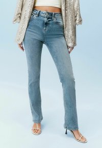 Lyseblå højtaljede jeans med lige ben, der har to forlommer og diskret udvaskning, kombineret med hvide stroppestøvler.