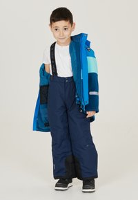 Blauwe winterjas in verschillende tinten; met rits en capuchon. Donkerblauwe sneeuwbroek met verstelbare bandjes; gladde textuur en gevoerd ontwerp.