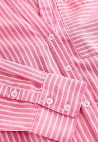 Pink striped button-up shirt featuring white stripes, long sleeves, and white buttons with visible stitching details and a chest pocket.