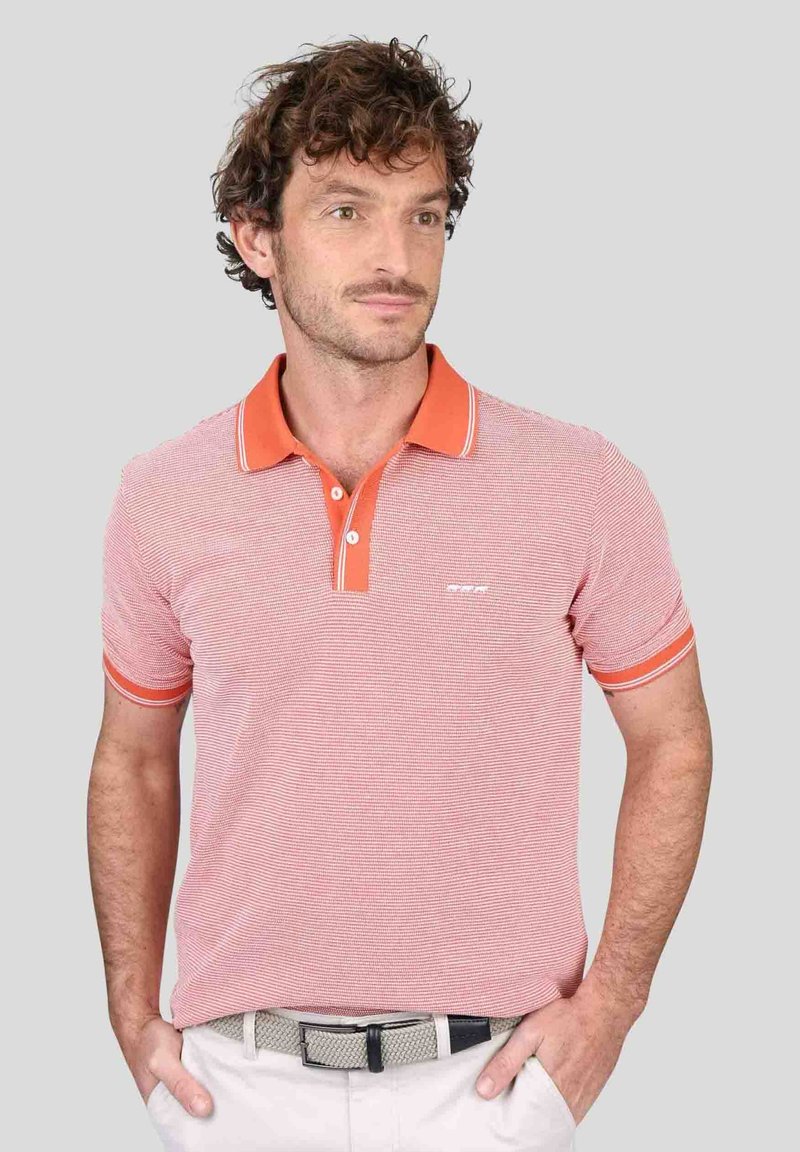 Polo rayé rouge et blanc avec un col et des accents de manche orange. Il présente une patte de boutonnage à deux boutons et un petit logo sur la poitrine.
