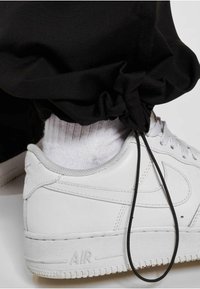 Hvide lædersneakers med grå accenter, parret med en sort opsmøgning på buksebenet. En sort snor er synlig nær anklen, sammen med en hvid sok.