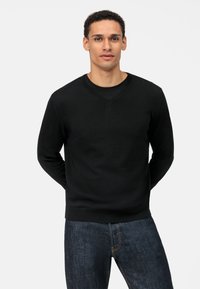 Zwarte v-hals trui van een gladde breiselstof, met een nauwsluitende pasvorm en lange mouwen, gecombineerd met donkerdenim jeans.