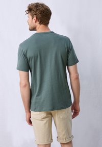 Grön kortärmad T-shirt med rund halsringning, slät textur och avslappnad passform, matchad med beige uppvikta shorts.