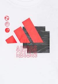 Hvit t-skjorte med røde og svarte Adidas-logoer med geometriske former og tre kuleikoner over i rødt, trykket på mykt bomullsmateriale.
