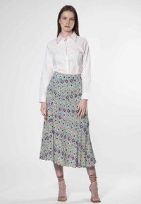 Chemise blanche à boutons avec col, assortie à une jupe midi à motifs présentant des formes géométriques en bleu, rose, jaune et vert.