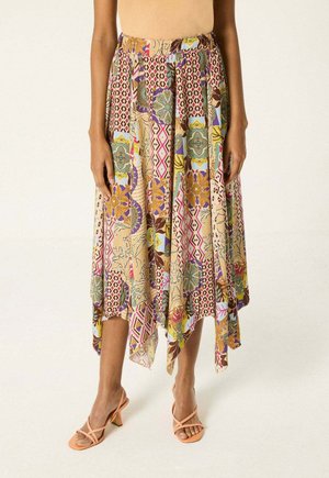 Mujer con una falda midi suelta y multicolor con patrones geométricos y florales combinada con sandalias de tacón con tiras en color melocotón.