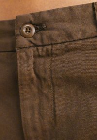 Brun bomullstyg med knäppning och synlig textur. Inkluderar söm detaljer längs sömmen.