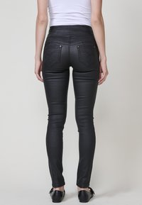 Jeans negros de tiro alto con una textura suave y elástica. Presenta dos bolsillos traseros con costuras decorativas. Ajuste slim desde la cintura hasta el tobillo.