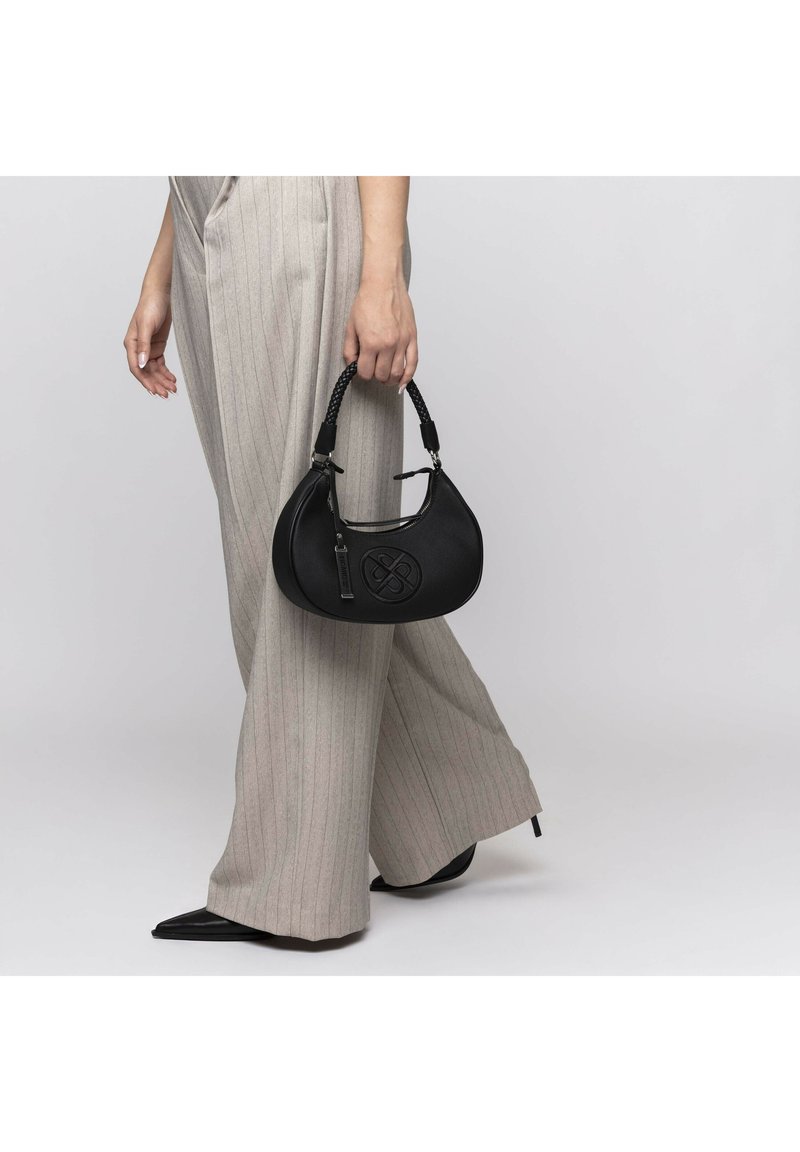 Black leather handbag with a textured surface and woven handle, featuring a central logo and silver hardware, held in a hand wearing striped pants.
