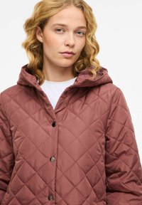 Quiltet rosa jakke med hette, utstyrt med trykknapper og en glatt, blank overflate. Designet inkluderer diamantformet søm.