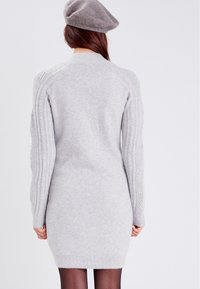 Robe en maille grise avec des manches côtelées, une silhouette ajustée et un ourlet arrondi. Comprend un béret gris assorti. Texture douce.