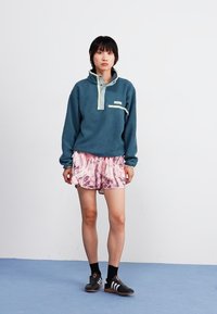Blue fleece pullover with a buttoned collar, cream accents, and a front pocket, paired with pink patterned shorts and black socks.