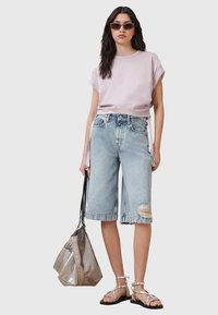 Top corto a maniche corte di colore viola chiaro, pantaloni Bermuda in denim chiaro sbiadito, borsa metallizzata argentata e sandali argentati con cinturini.