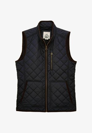 Navy sininen tilkkutäkki ilman hiuksia liivi ruskeilla korostuksilla, etuvetoketju, kaksi ala-taskua ja yksi vetoketjullinen rintatasku.