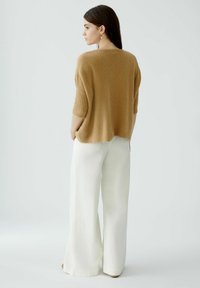 Beige Strickpullover mit kurzen, gerippten Ärmeln, kombiniert mit weiten weißen Hosen. Das Outfit besticht durch einen lässigen Schnitt und weiche Texturen.