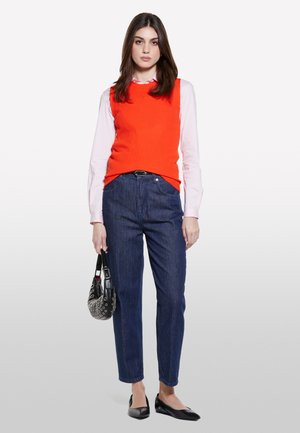 Orange ribbed sleeveless sweater over a pink shirt, paired with dark blue denim jeans and black flats, holding a patterned handbag.