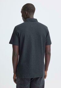 Donkergrijs poloshirt met een gestructureerde stof, korte mouwen en een klassieke kraag. De zoom is aan de achterkant licht gebogen.