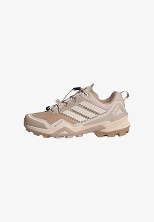 Lichtbeige outdoorschoen met een ademende bovenkant van mesh, een geometrisch patroon, versterkte neus en een rubberen zool met diepe profielen voor grip.