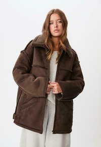 Giacca marrone, oversize, realizzata in morbido suede sintetico con colletto in pile, dotata di due tasche frontali e chiusura con zip.