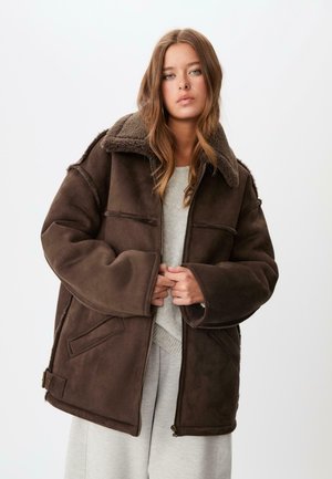Veste marron surdimensionnée en doux cuir synthétique avec un col en polaire, comportant deux poches frontales et une fermeture éclair.