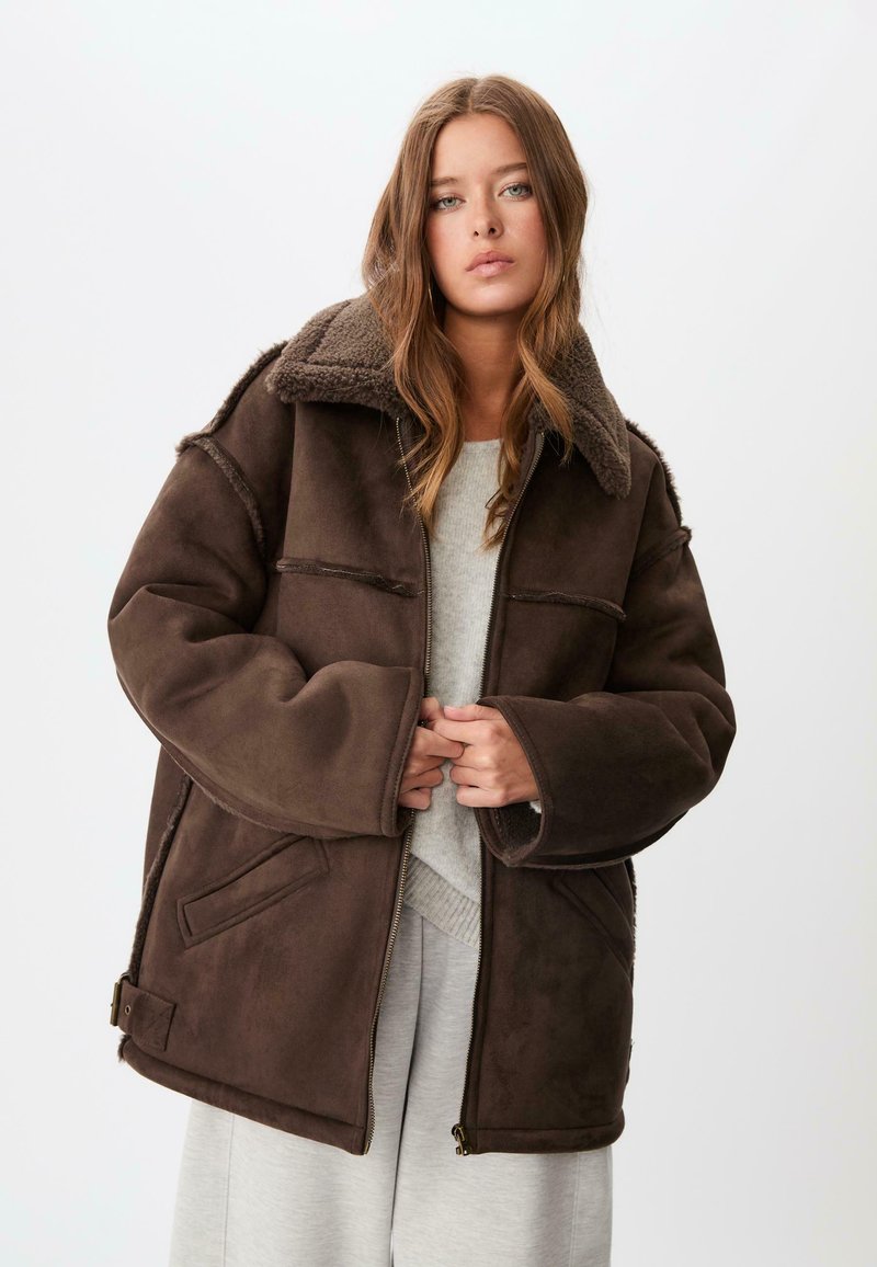 Giacca marrone, oversize, realizzata in morbido suede sintetico con colletto in pile, dotata di due tasche frontali e chiusura con zip.