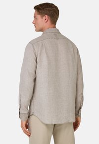 Camicia a maniche lunghe color beige chiaro con colletto all'americana, orlo curvo e dettagli di cucitura visibili. Il tessuto appare testurizzato e simile al lino.