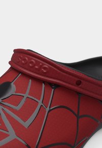 Κοντινή λήψη κόκκινου και μαύρου παπουτσιού τύπου τσόκ με σχέδιο ιστού αράχνης και ρυθμιζόμενο λουράκι με ανάγλυφο κείμενο.