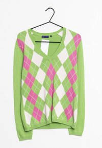 Grön V-ringad tröja med ett diamantmönster i rosa och vitt. Har en stickad struktur och långa ärmar. Hänger på en svart krok.