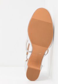 Sandale argentée à talon haut avec une semelle en caoutchouc texturée couleur beige, une tige synthétique et de fines brides à la cheville. Présente un design élégant et minimaliste.