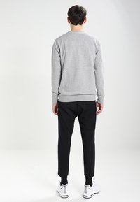 Grå sweatshirt med rund hals, ribbede ærmegab og linning, kombineret med sorte taperede bukser og hvide sneakers.