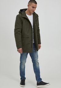 Olivengrønn parka-jakke med hette, med frontglidelås og trykknapplukking, store frontlommer og kontrastfôring.