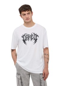 Biała bawełniana koszulka z krótkim rękawem, z czarnym wzorem graficznym z napisem "Dare" na piersi. Okrągły dekolt. Brak widocznych logo.