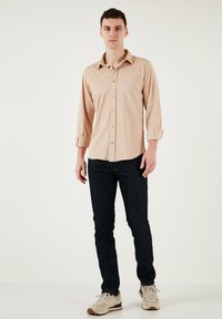 Beige, hosszú ujjú, gombos ing, felgöngyölt mandzsettával, puha textúrával. Sötét farmernadrággal és világos színű tornacipővel párosítva. Egyszerű dizájn.