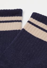 Chaussettes bleu marine avec des rayures beiges en haut, fabriquées dans un matériau tricoté doux, dotées d'un bord côtelé et d'une texture lisse.
