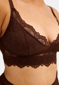 Brun spetsbralette med djup V-ringning, scallopade kanter och blommönster. Mjuk textur med justerbara band för bättre passform.