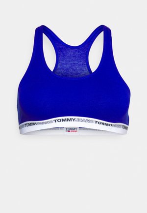 Mėlynas sportinis liemenukas, pagamintas iš tamprios medžiagos, su lenktu nugaros dizainu ir baltu elastiniu juostu, ant kurio yra užrašyta "TOMMY JEANS".