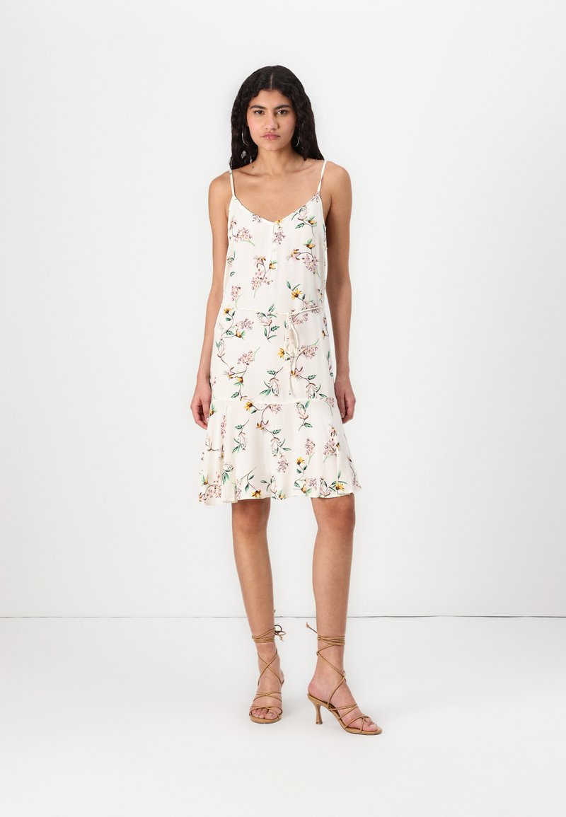 Rochie albă cu imprimeu floral, cu bretele subțiri, față cu nasturi și tiv în straturi. Materialul pare ușor și respirabil.