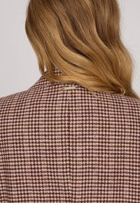 Blazer en mélange de laine avec un motif pied-de-poule marron et rose, doté d'un col montant et de détails matériels subtils à l'arrière.