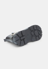 Suela de bota negra con surcos profundos para tracción, forma curvada y material de goma reforzada. Presenta un detalle circular liso central.