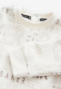 Sweat-shirt couleur crème présentant un motif de logo répété en marron clair. Poignets et col côtelés, tissu en coton doux, coupe décontractée.