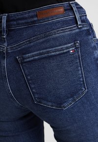 Jeans de mezclilla azul oscuro con un diseño de tiro medio, que presentan una etiqueta de cuero, costuras en contraste y un bolsillo trasero clásico con detalle del logo.