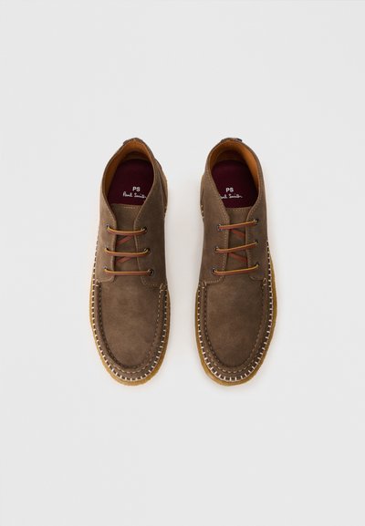 Chaussures en suede marron avec un bout rond, présentant des coutures contrastées, des lacets marron et un design simple. Semelle en caoutchouc et doublure en cuir.