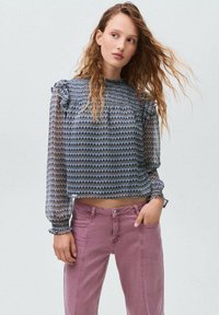 Blusa a maniche lunghe in tessuto trasparente con motivo, caratterizzata da dettagli a volant alle spalle, abbinata a jeans in denim rosa chiaro a vita alta.