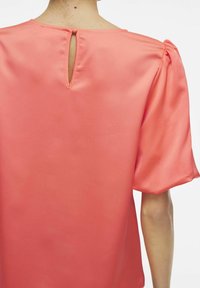 Top in satin corallo con un'apertura a chiave sulla schiena, maniche corte a sbuffo e una texture liscia.